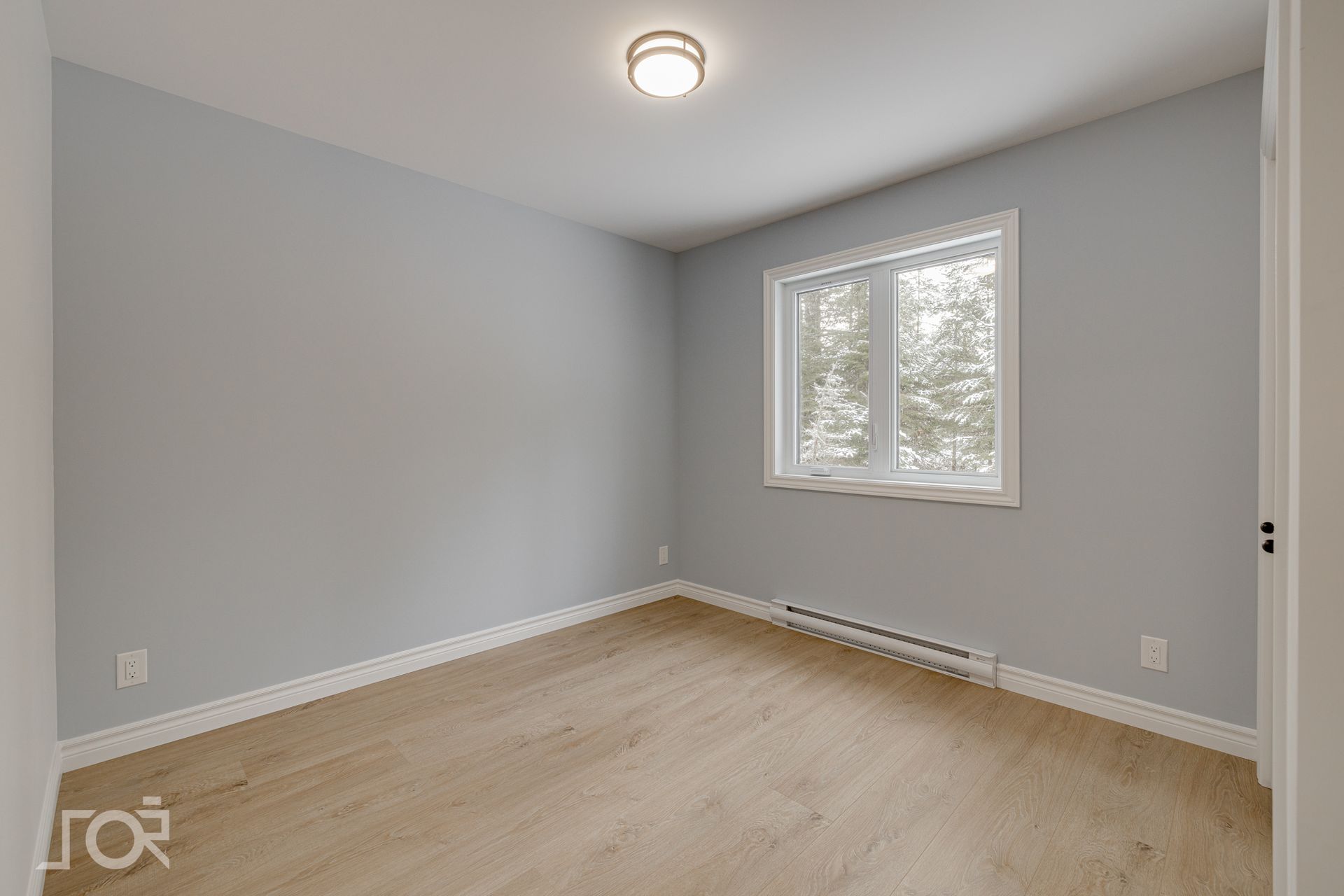 Pièce vide aux murs bleu clair, avec une fenêtre et un parquet. Un plafonnier éclaire l'espace.