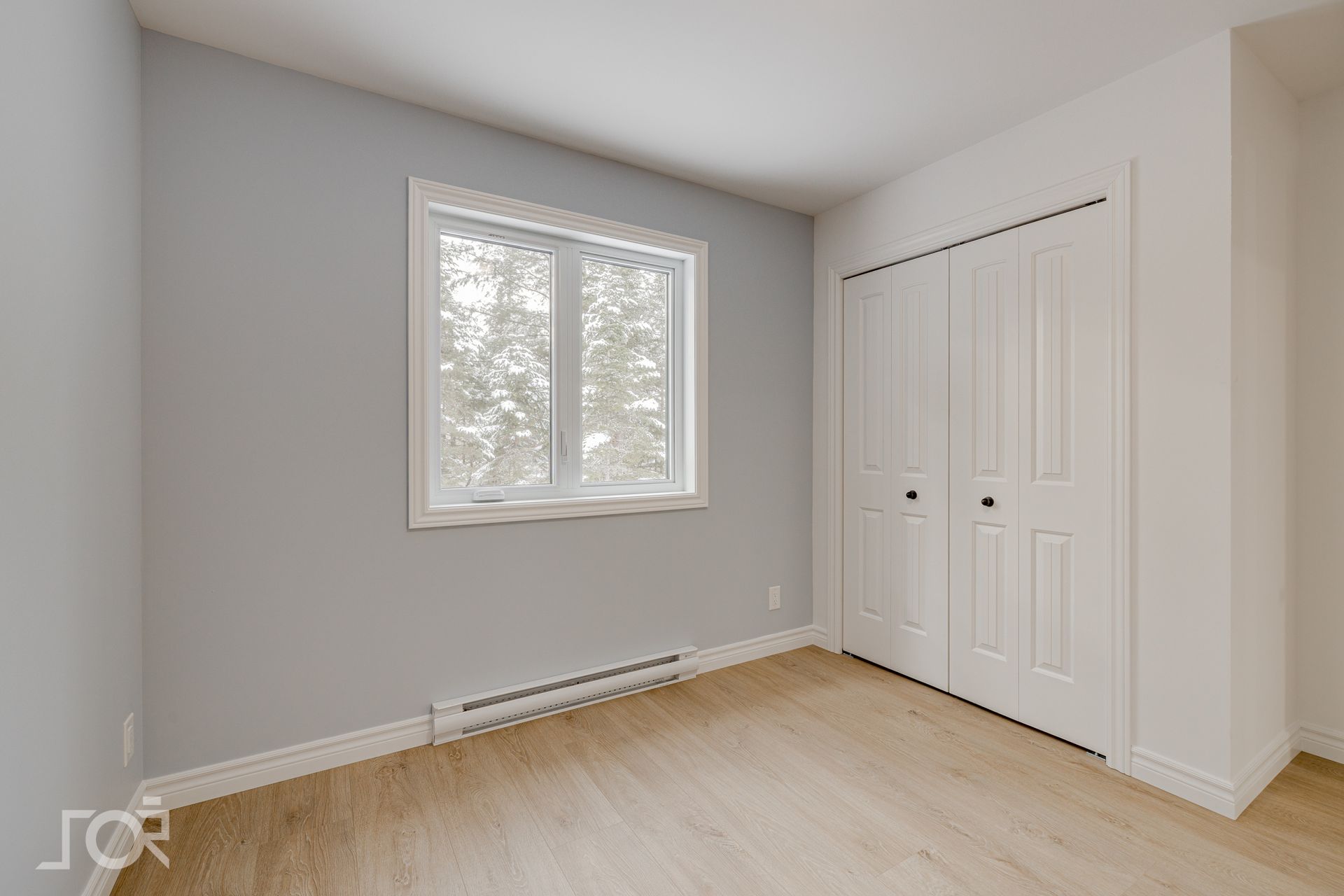 Chambre vide avec parquet clair, murs gris, placard blanc et fenêtre.