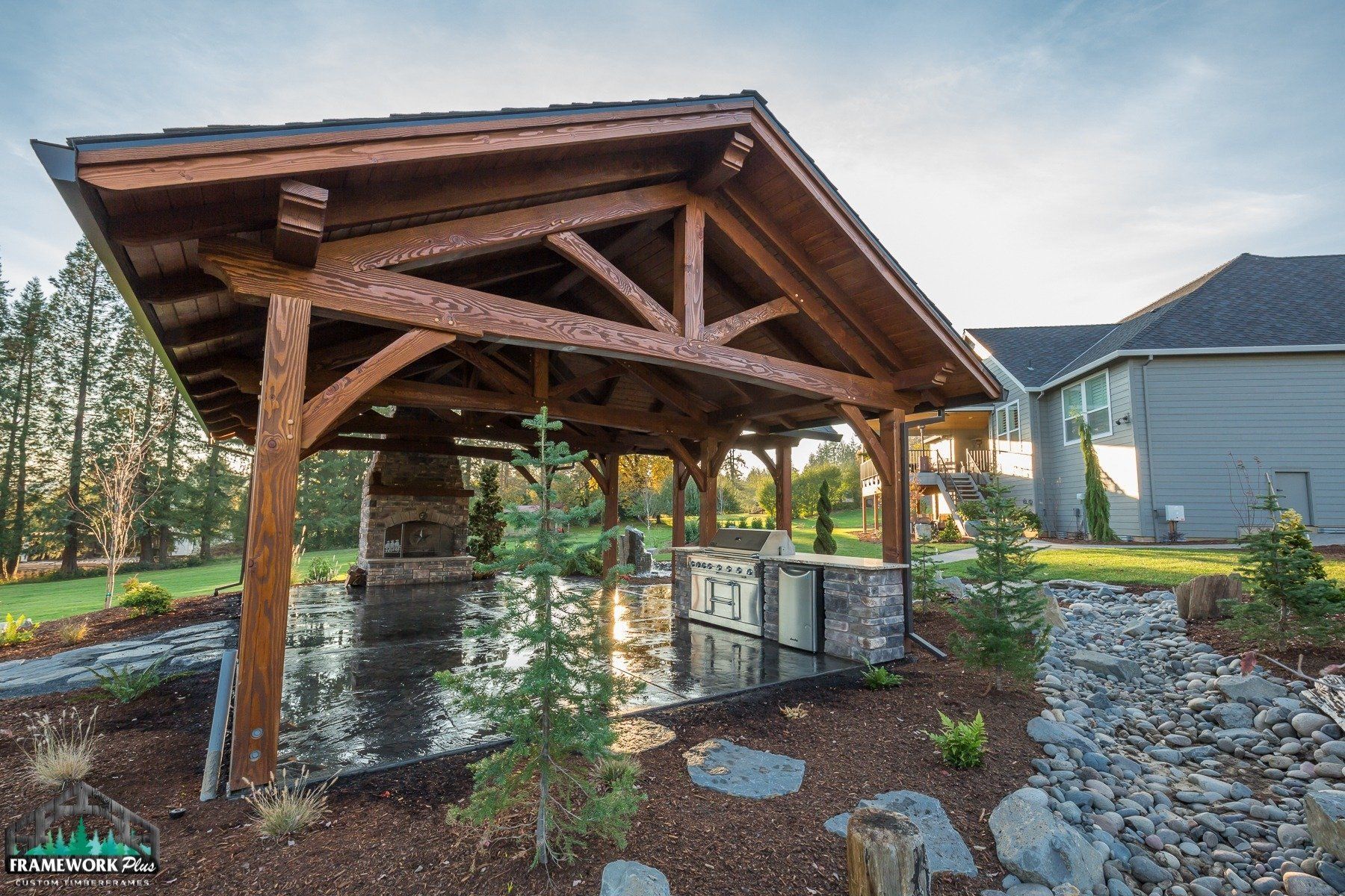 A wooden pavilion with a fireplace in the backyard of a house.