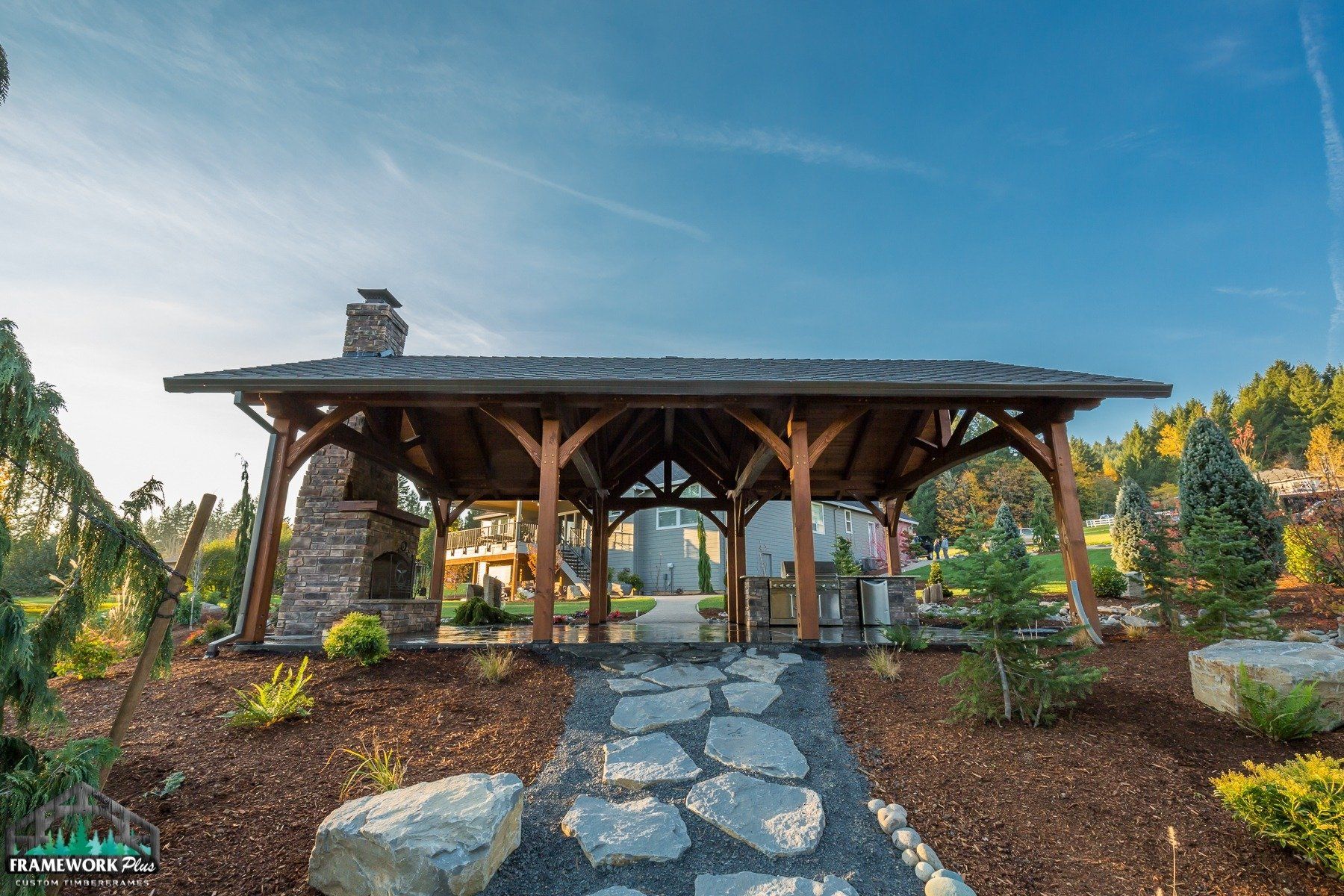 A wooden pavilion with a stone fireplace is surrounded by rocks and trees.