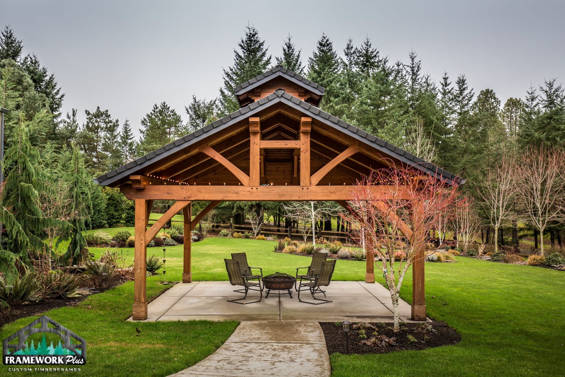 A wooden pavilion with a table and chairs in the middle of a lush green field.