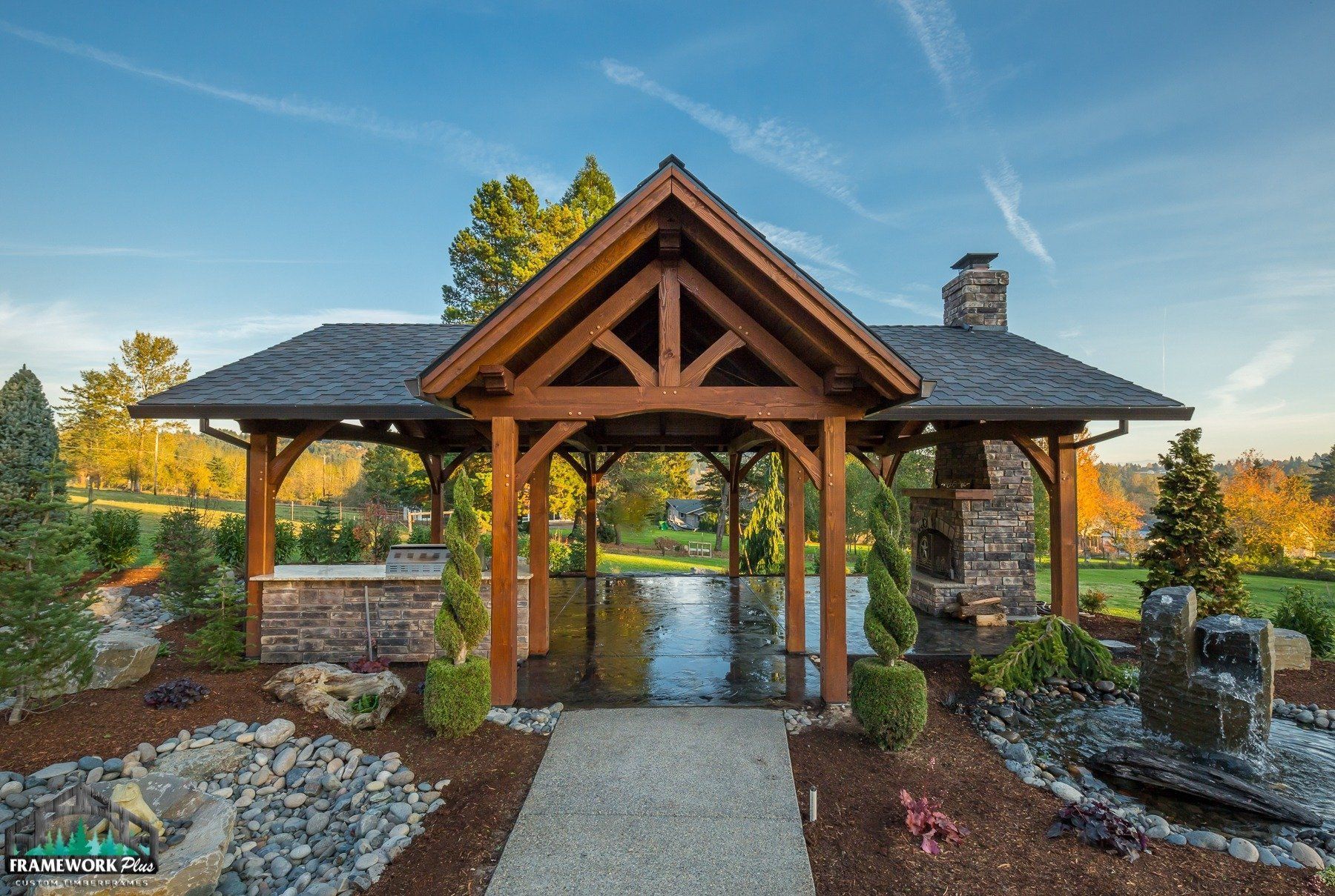 A large wooden pavilion with a gray roof is surrounded by rocks and trees.