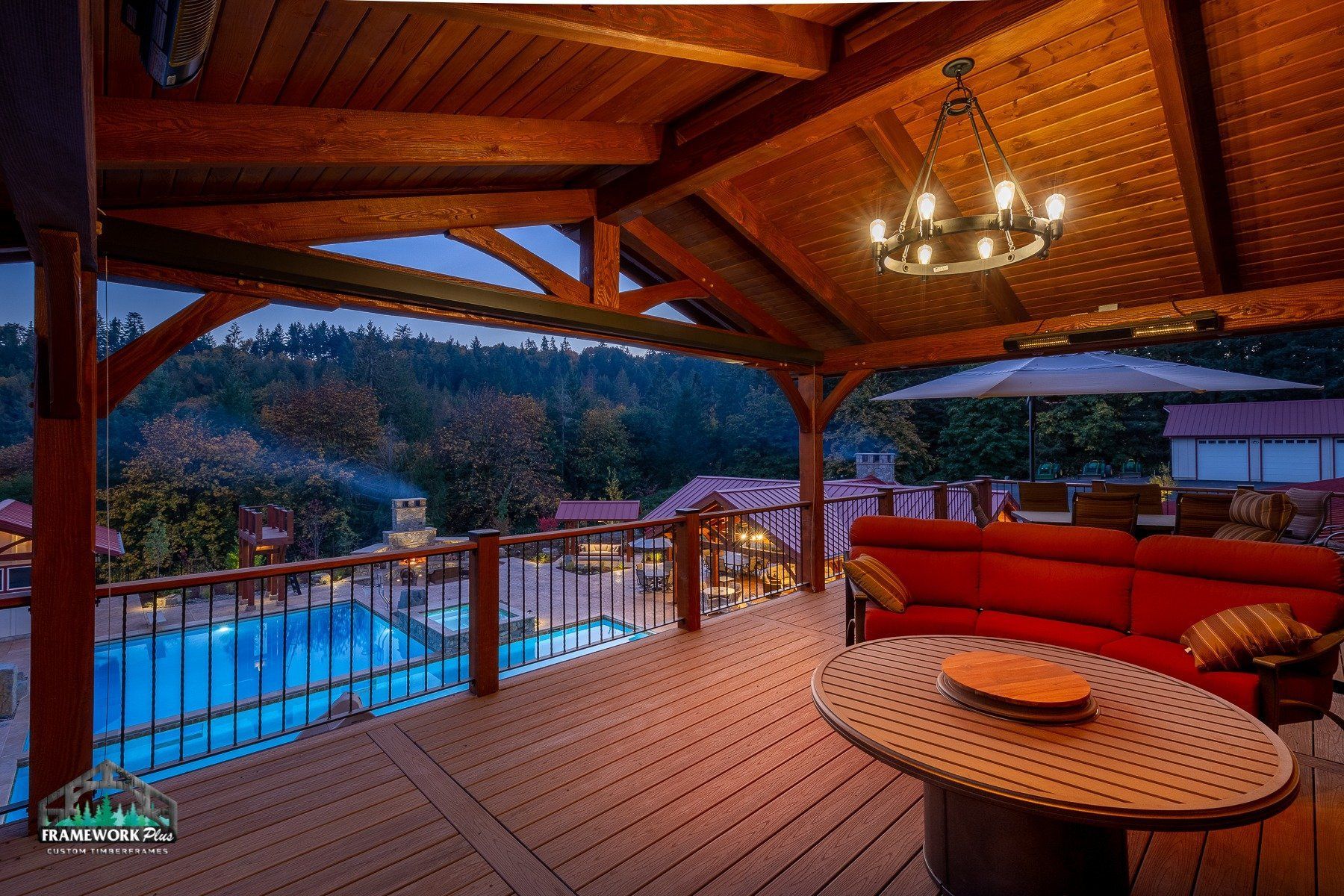 A wooden deck with a red couch and a table with a view of a swimming pool.