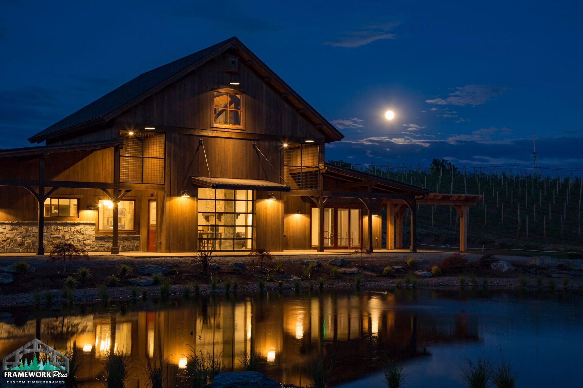 A barn is lit up at night with a full moon in the background.