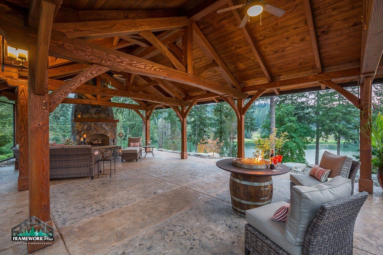 A large wooden pavilion with a fireplace , couch , chairs and a table.