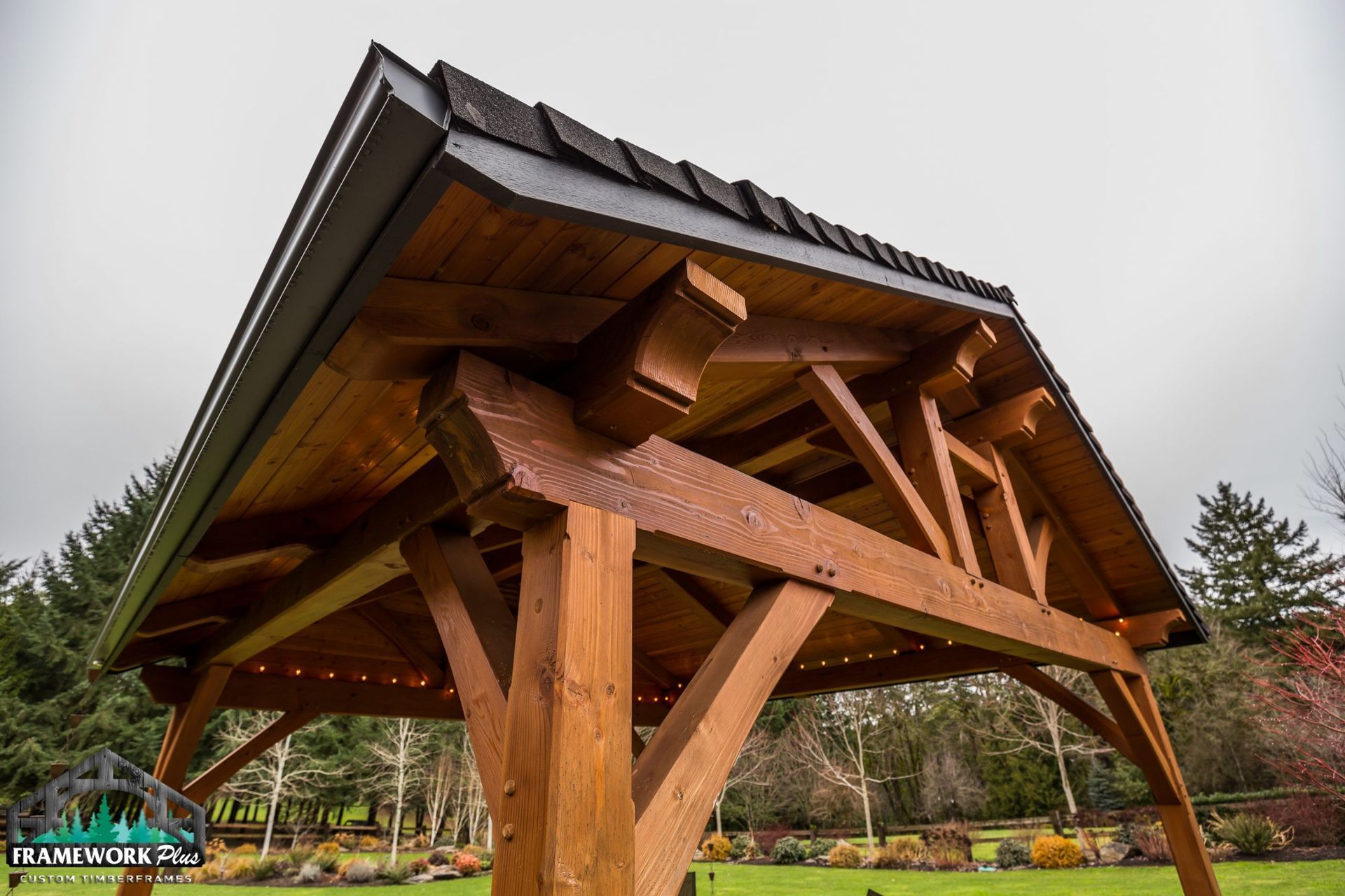 A wooden gazebo with a roof is sitting on top of a lush green field.