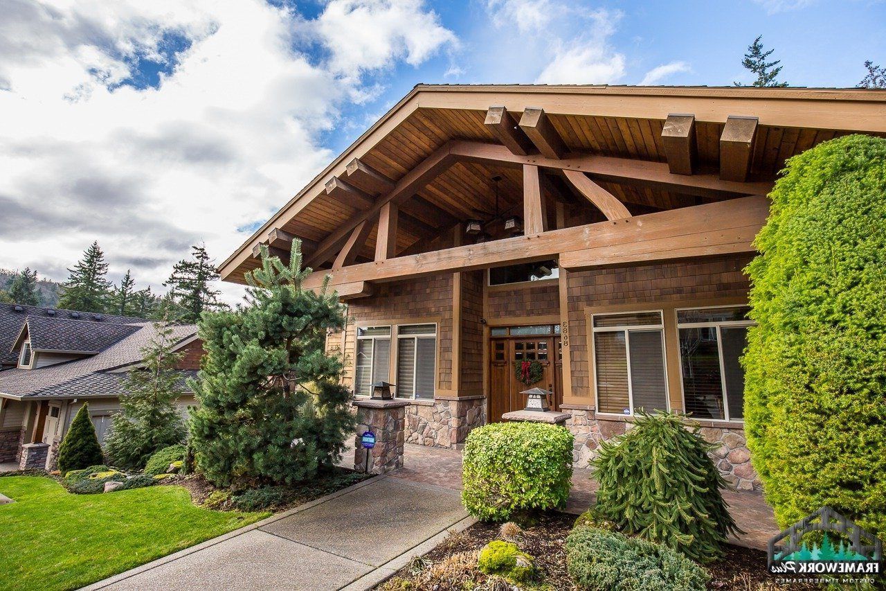 A large house with a wooden roof is surrounded by trees and bushes.