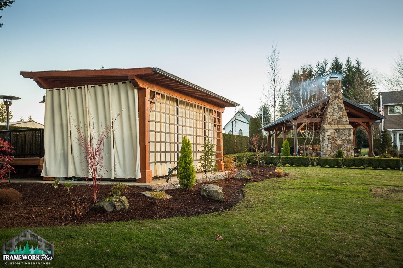 A wooden gazebo with white curtains is in the middle of a lush green yard.