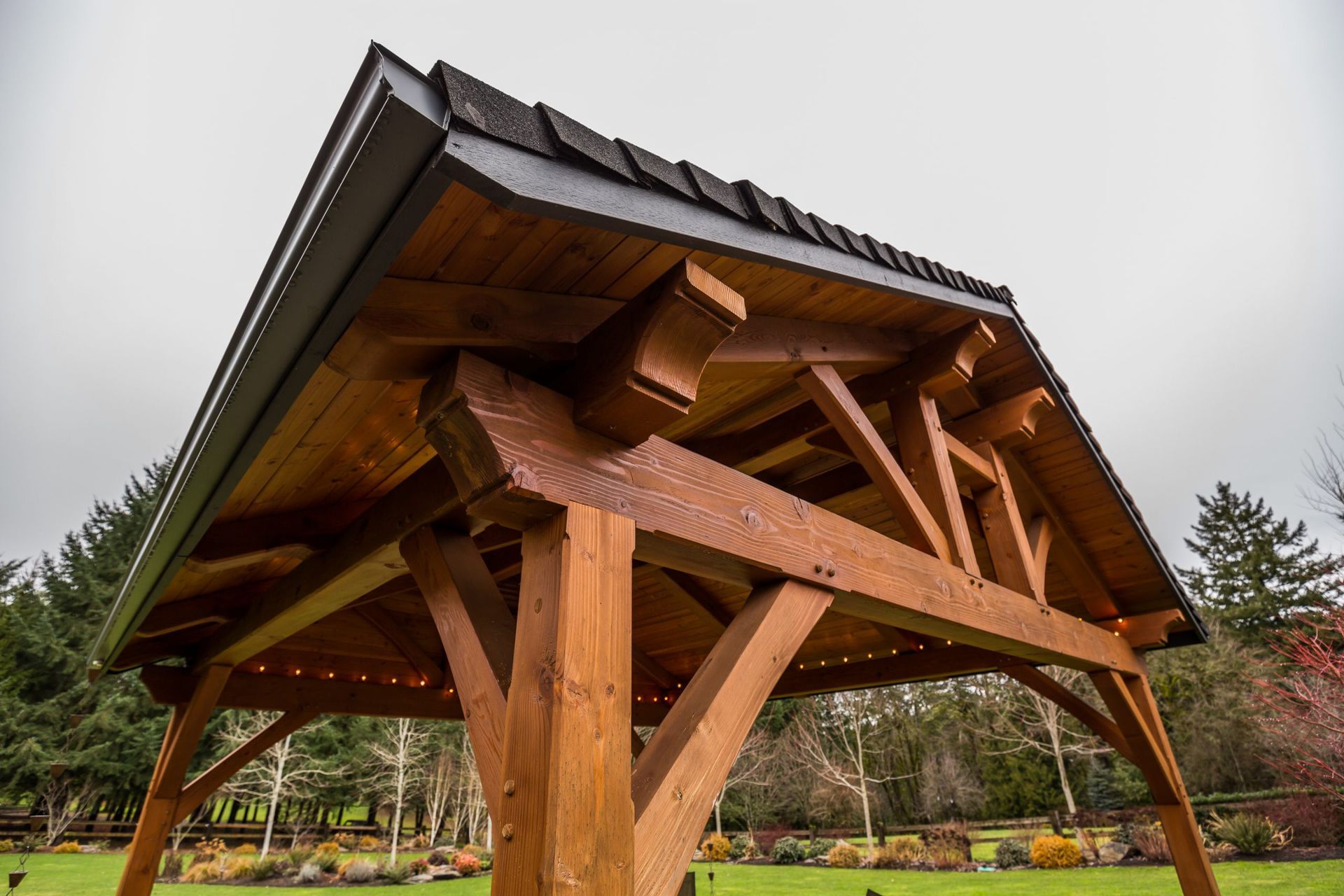 A wooden gazebo with a roof is sitting on top of a lush green field.