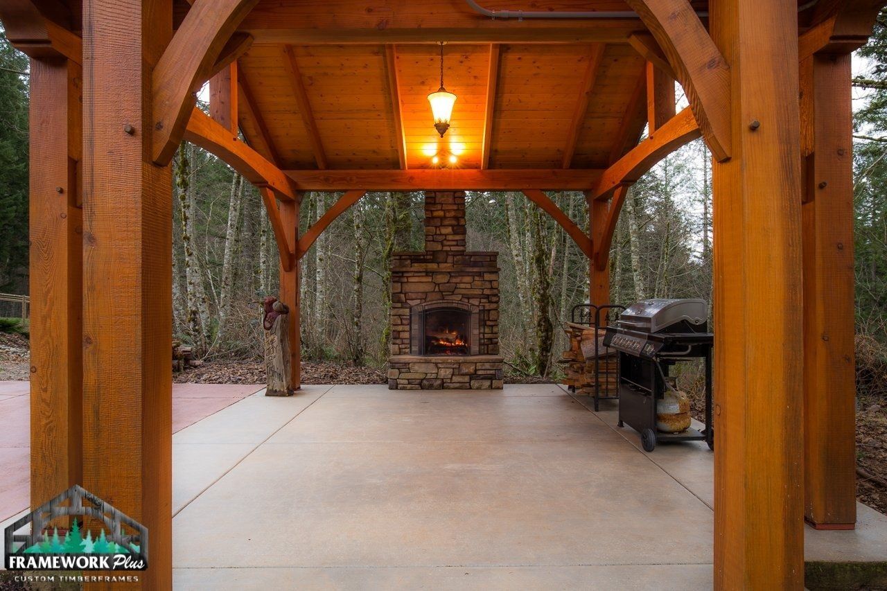 A wooden gazebo with a fireplace in the middle of it