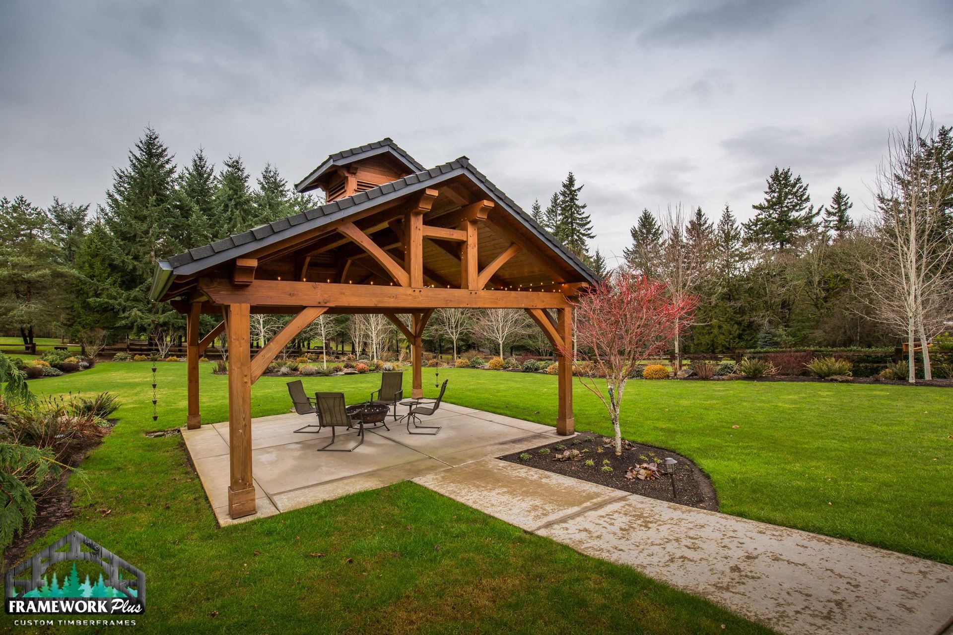 A wooden gazebo with a table and chairs in the middle of a lush green field.
