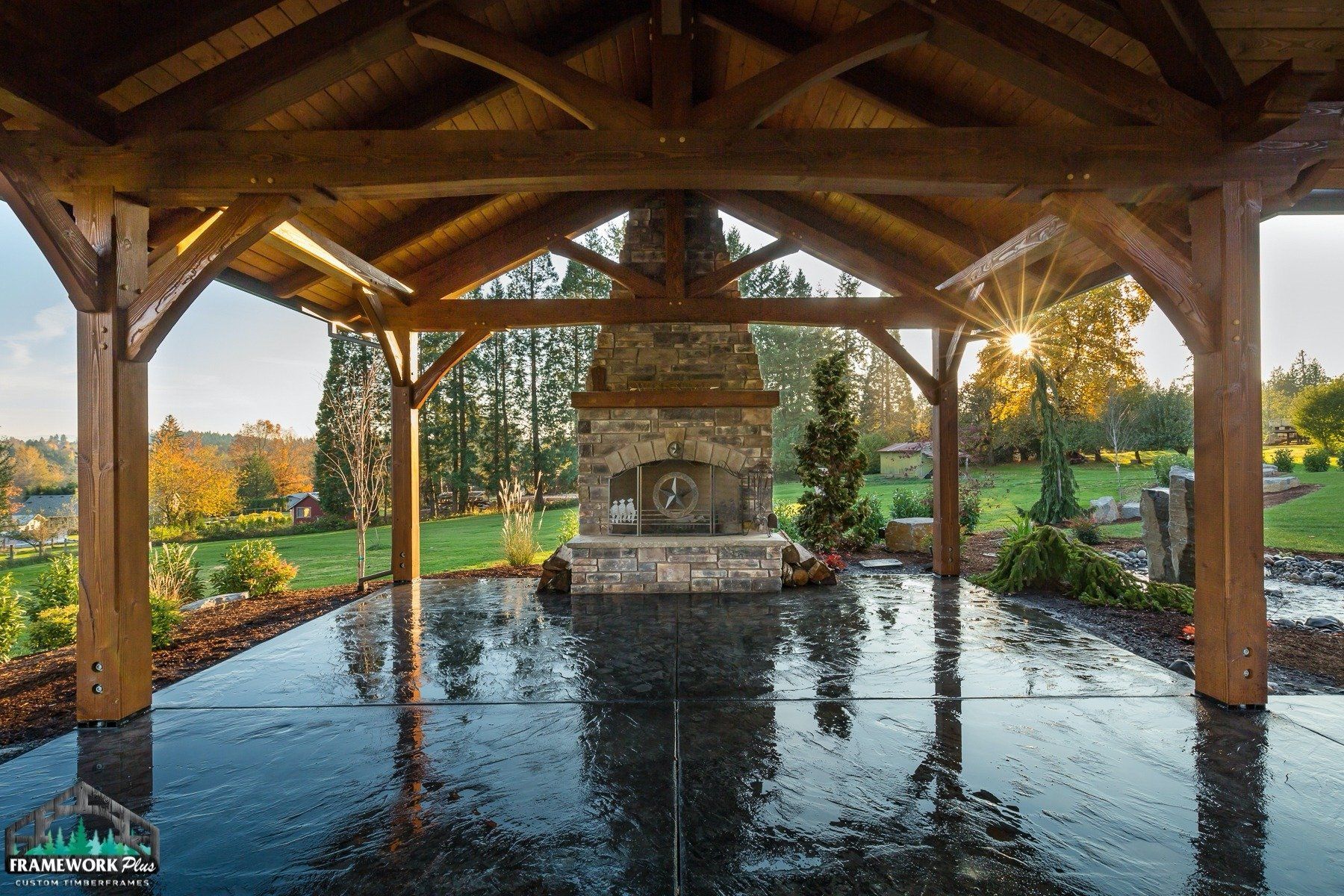 A wooden gazebo with a stone fireplace in the middle of it.