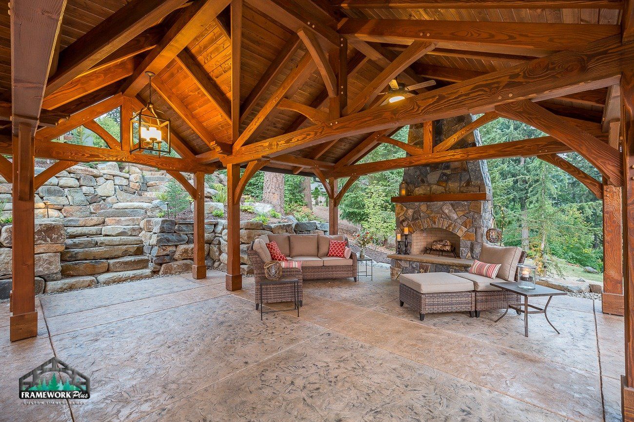 A wooden pavilion with a couch , chairs , and a fireplace.