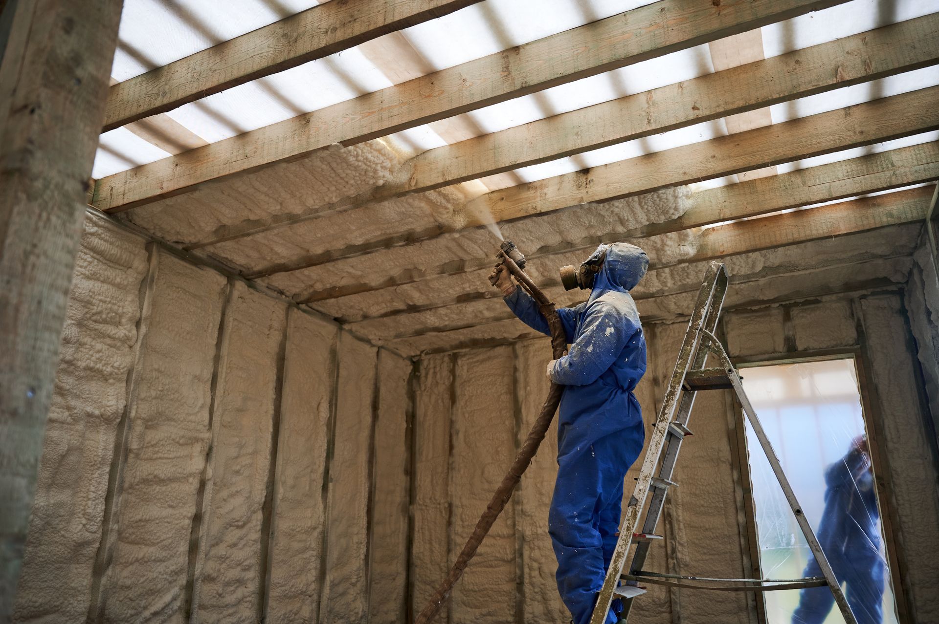 Installer applying spray foam insulation to overhead framing in a house.