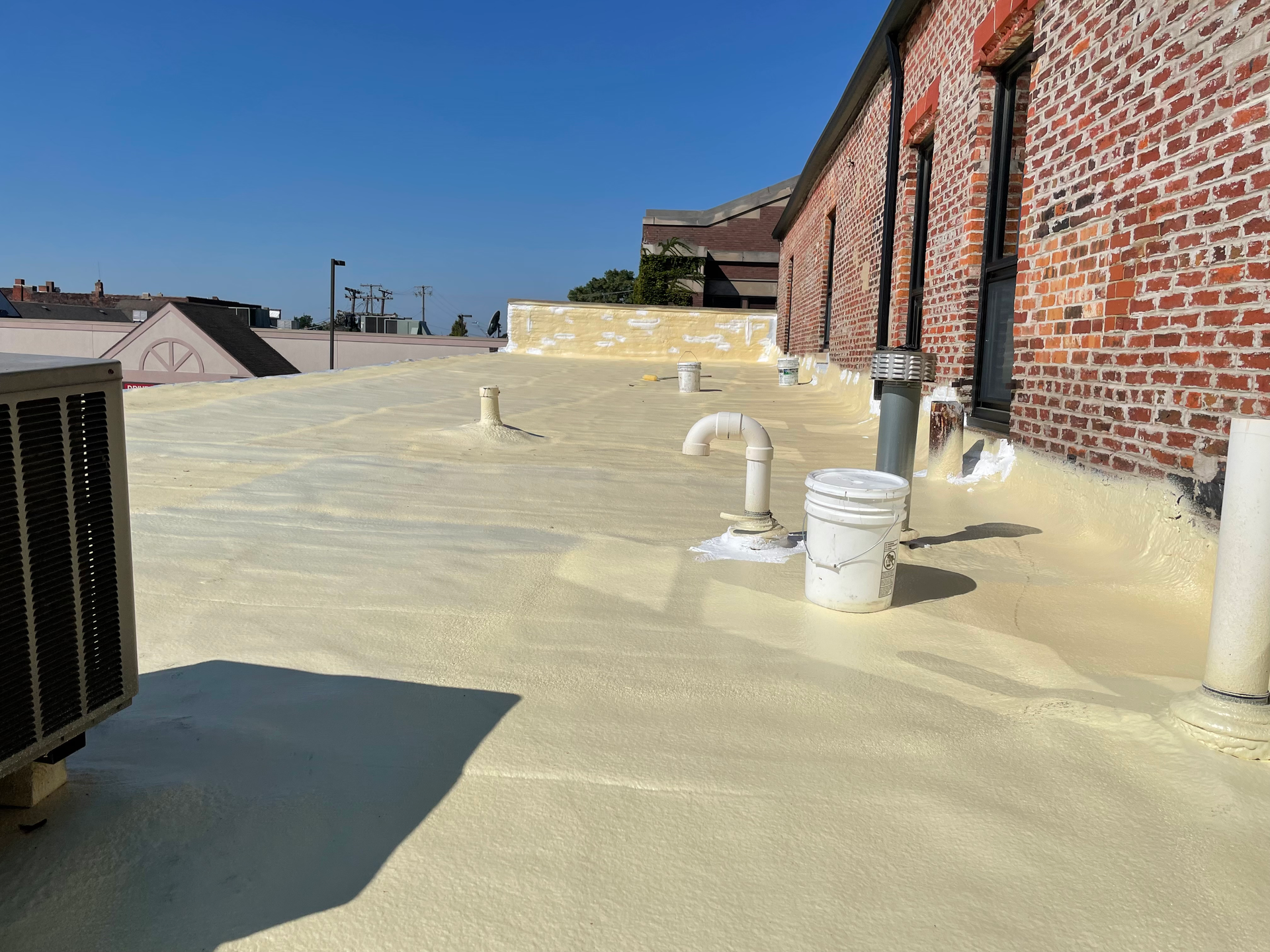 Rooftop with white waterproof coating, brick wall, HVAC units, and vents under a clear blue sky