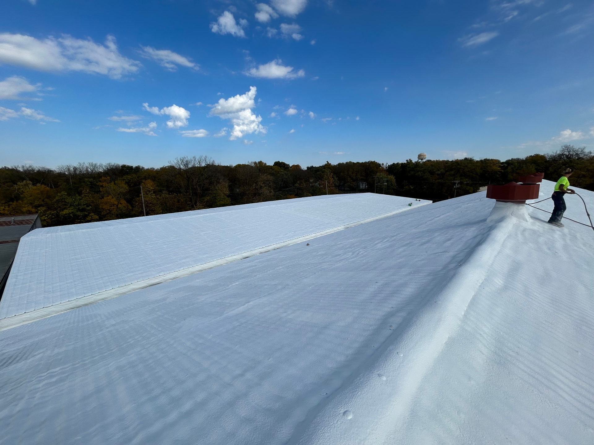 White roof under a blue sky, with a worker near a red vent on the right.