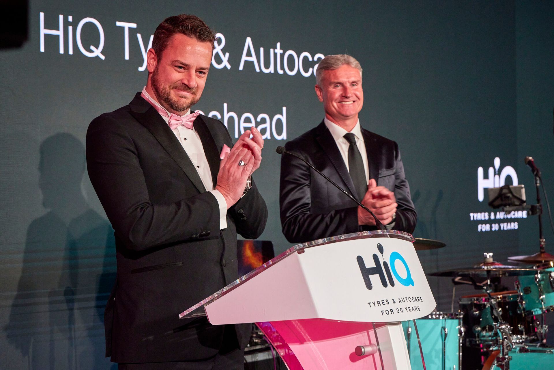 Two men in suits are standing at a podium and clapping.