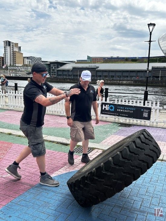 A man is helping another man lift a tire.