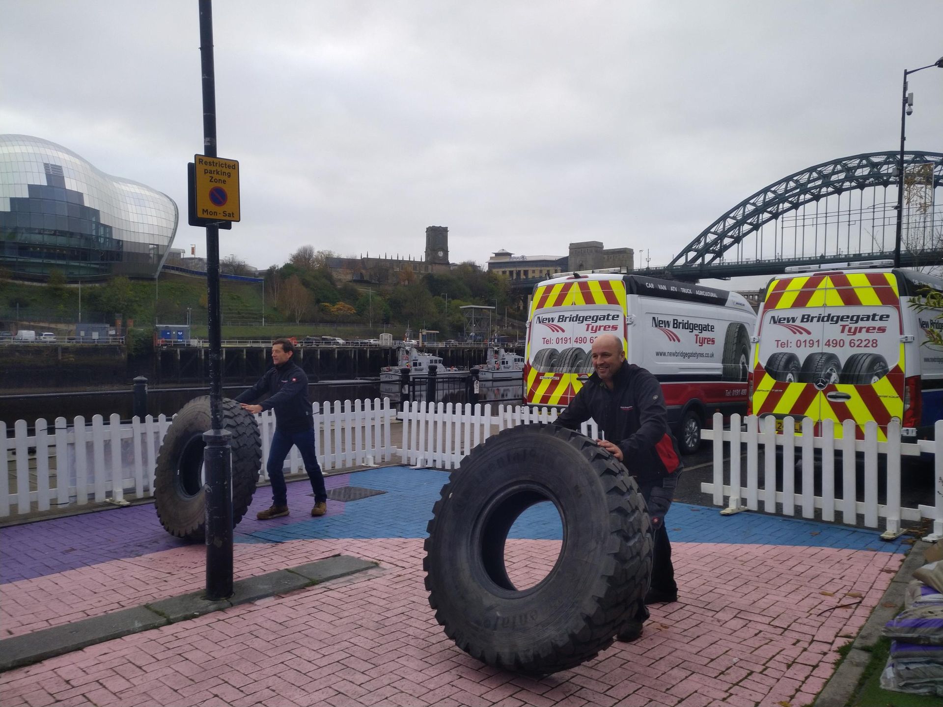 A man is pushing a large tire in a park.