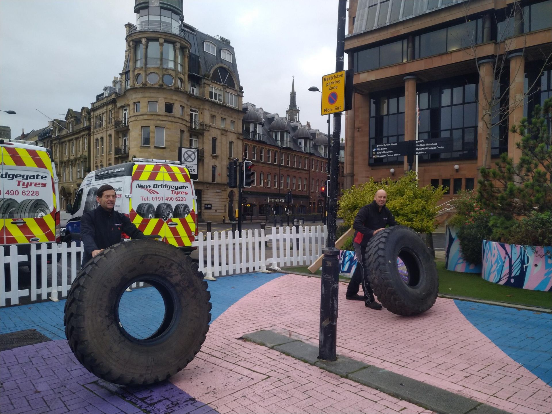 A man is pushing a large tire in a park.