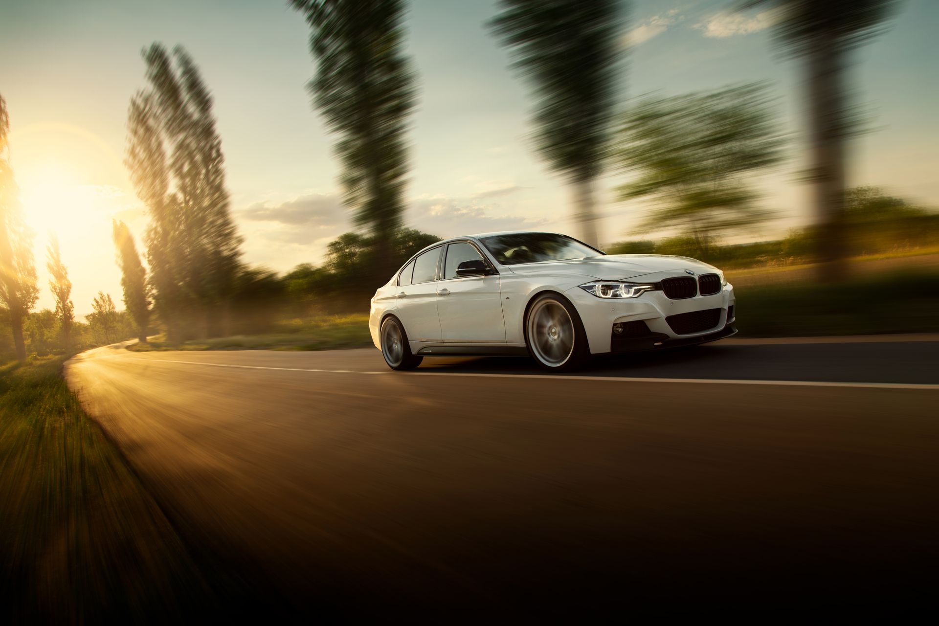 A white car is driving down a country road at sunset.