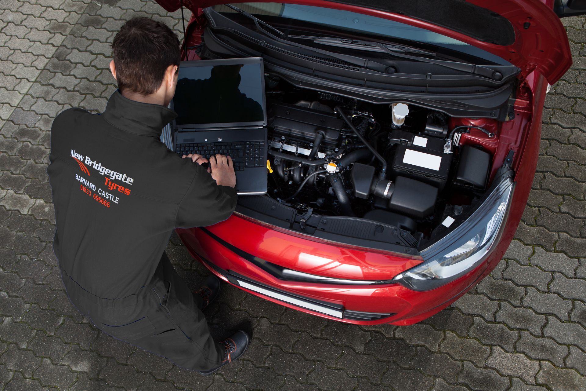 A man is working on the engine of a red car.