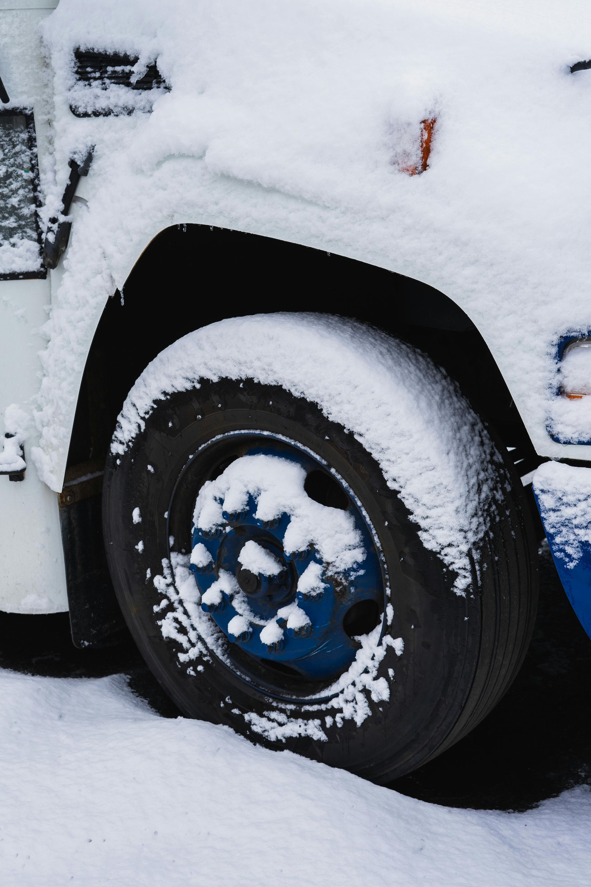 A white car with a blue wheel is covered in snow