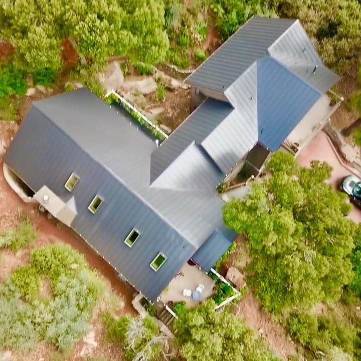 Overhead view of a modern house with a dark gray roof surrounded by trees and shrubbery.