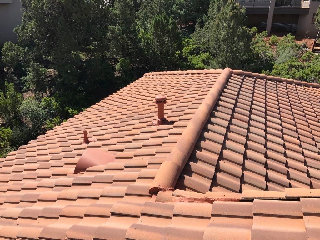 Brown tile roof with a vent and trees in the background.