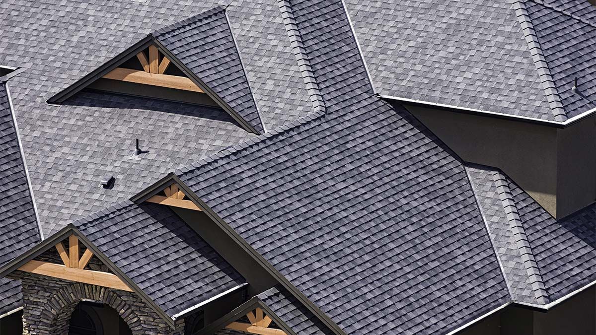 Gray asphalt shingle roof on a house, with gabled sections and wood trim.