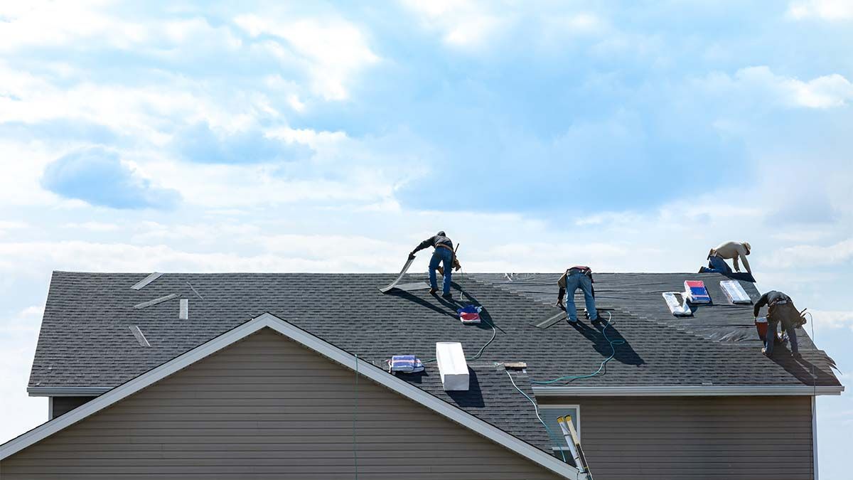 Roofers working on a house roof under a cloudy blue sky.