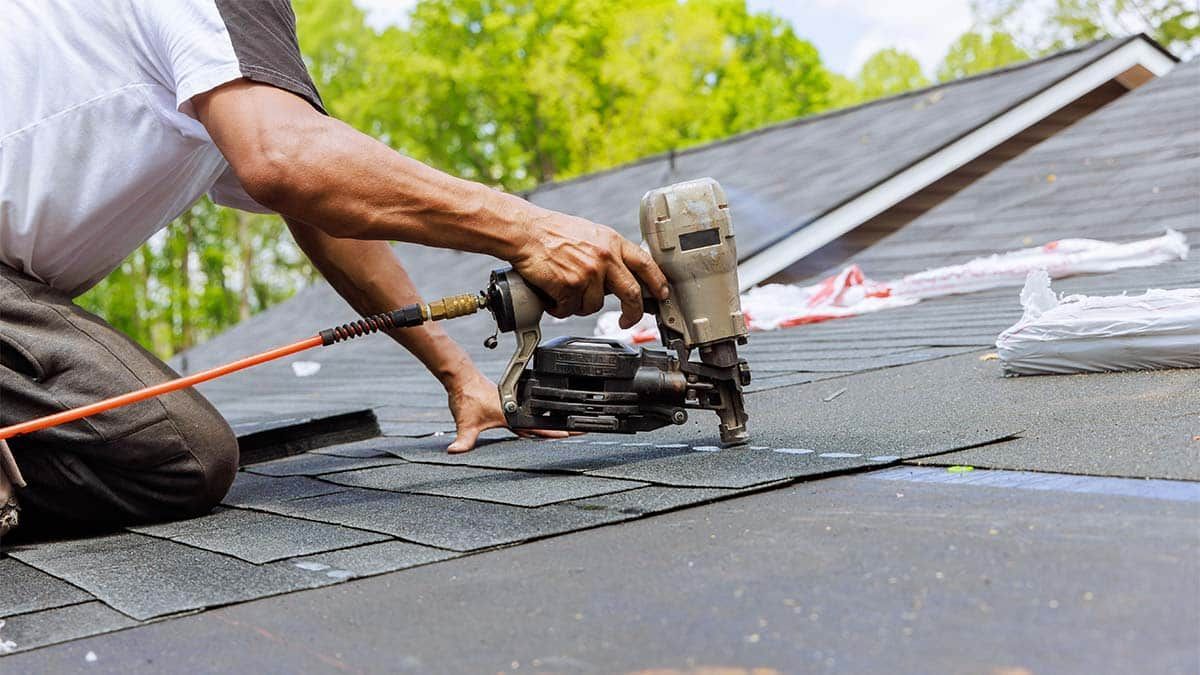 Roofer using a nail gun to attach shingles to a rooftop.