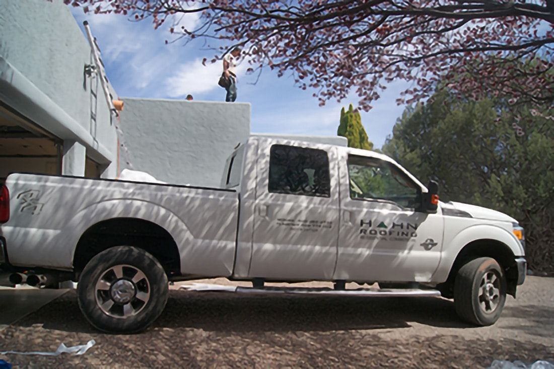 White pickup truck parked near a light blue building, with a person standing on a flat roof.
