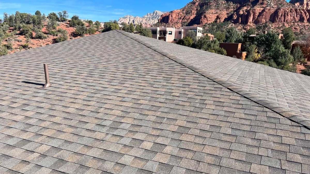 Roof of a building with brown and gray shingles, Sedona, Arizona, with red rock formations in the background.