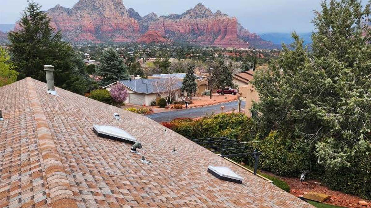 View of a brown roof with vents, overlooking a town with red rock mountains in the background.