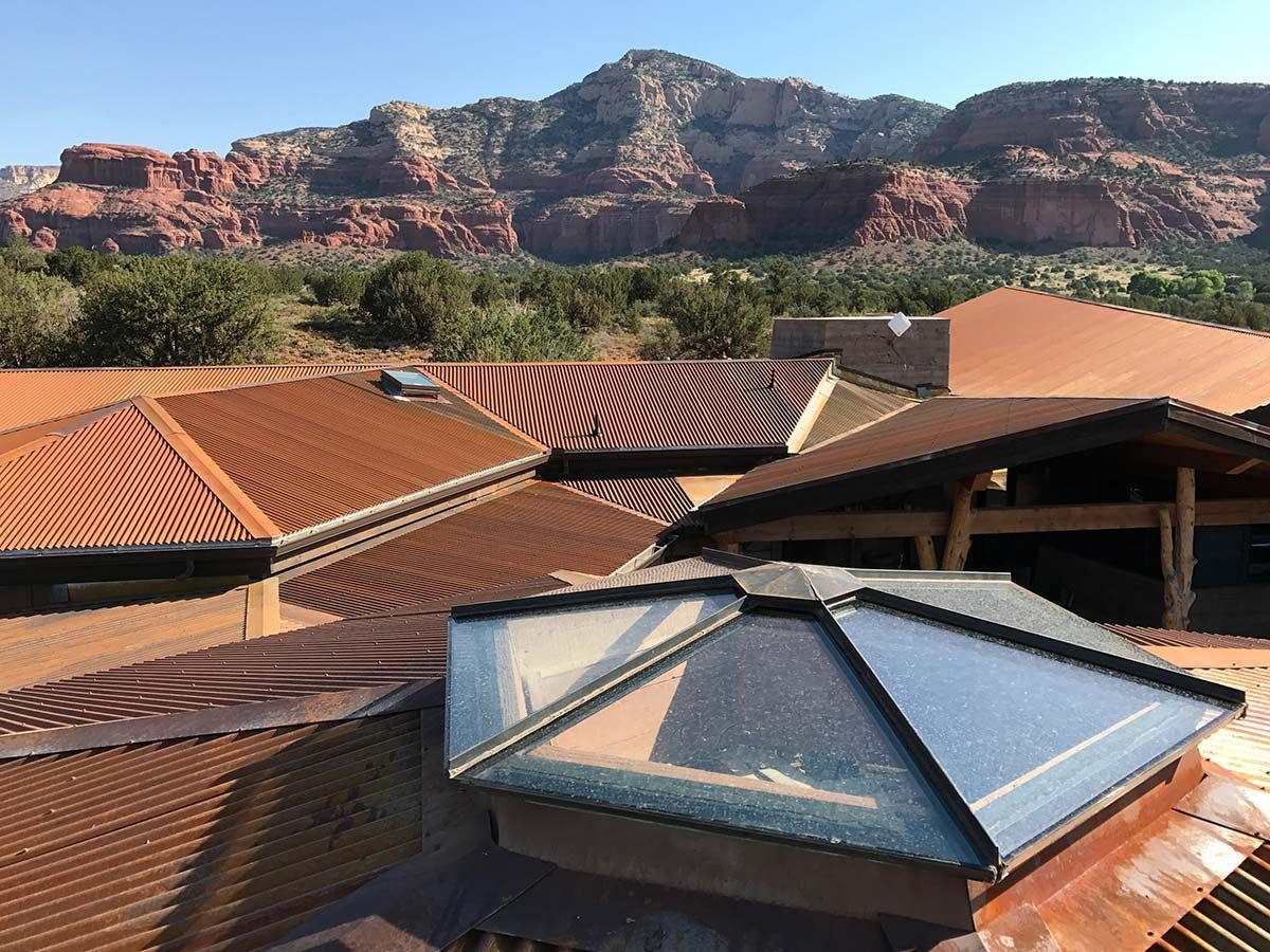 Rusty metal roofs with skylights against a backdrop of red rock mountains and blue sky.