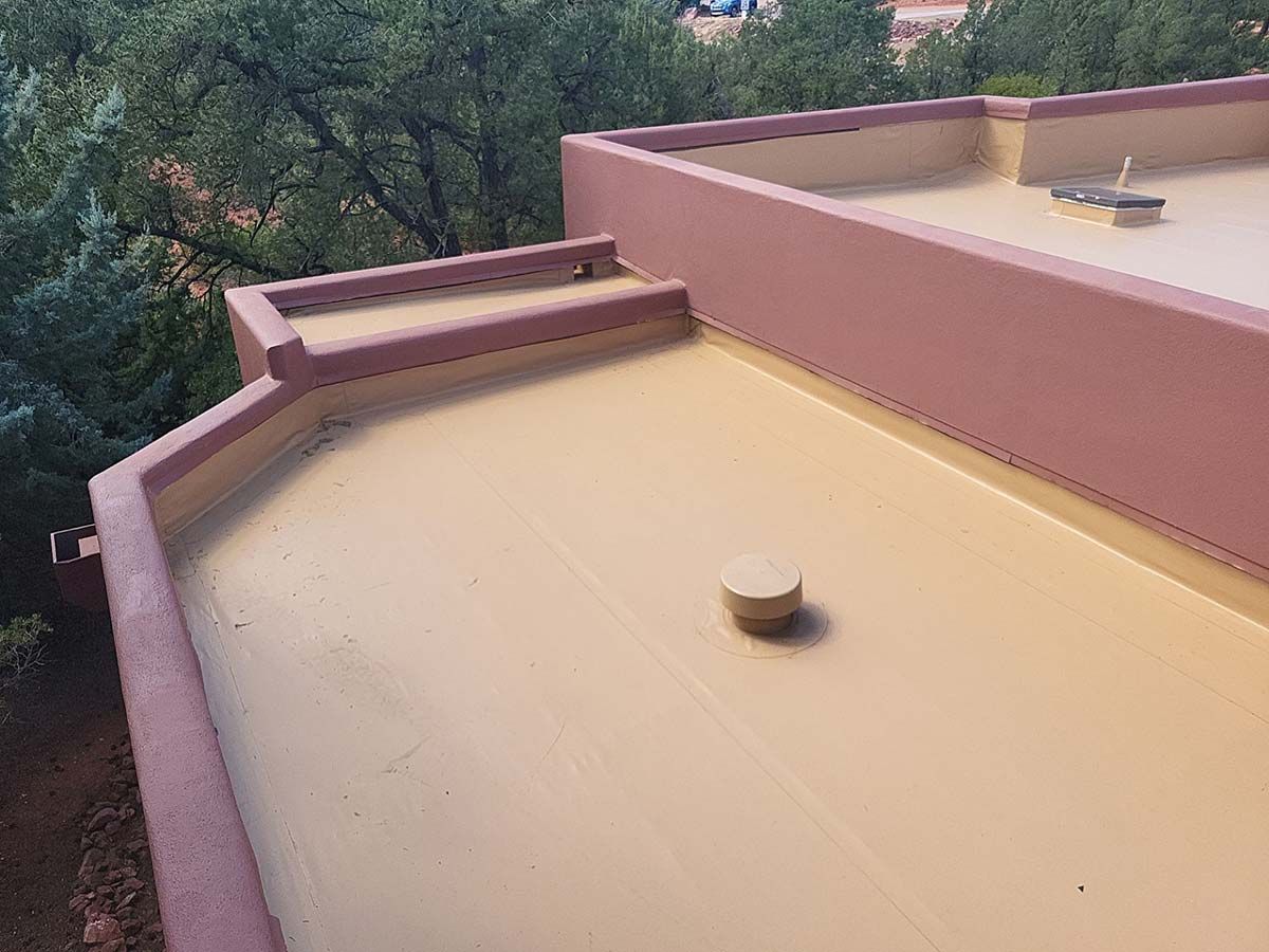 Flat roof with beige coating and brown trim; trees visible in the background.