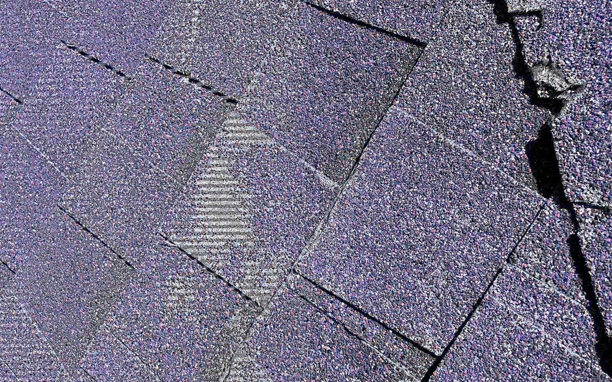Close-up of weathered purple asphalt roof shingles with some damage.