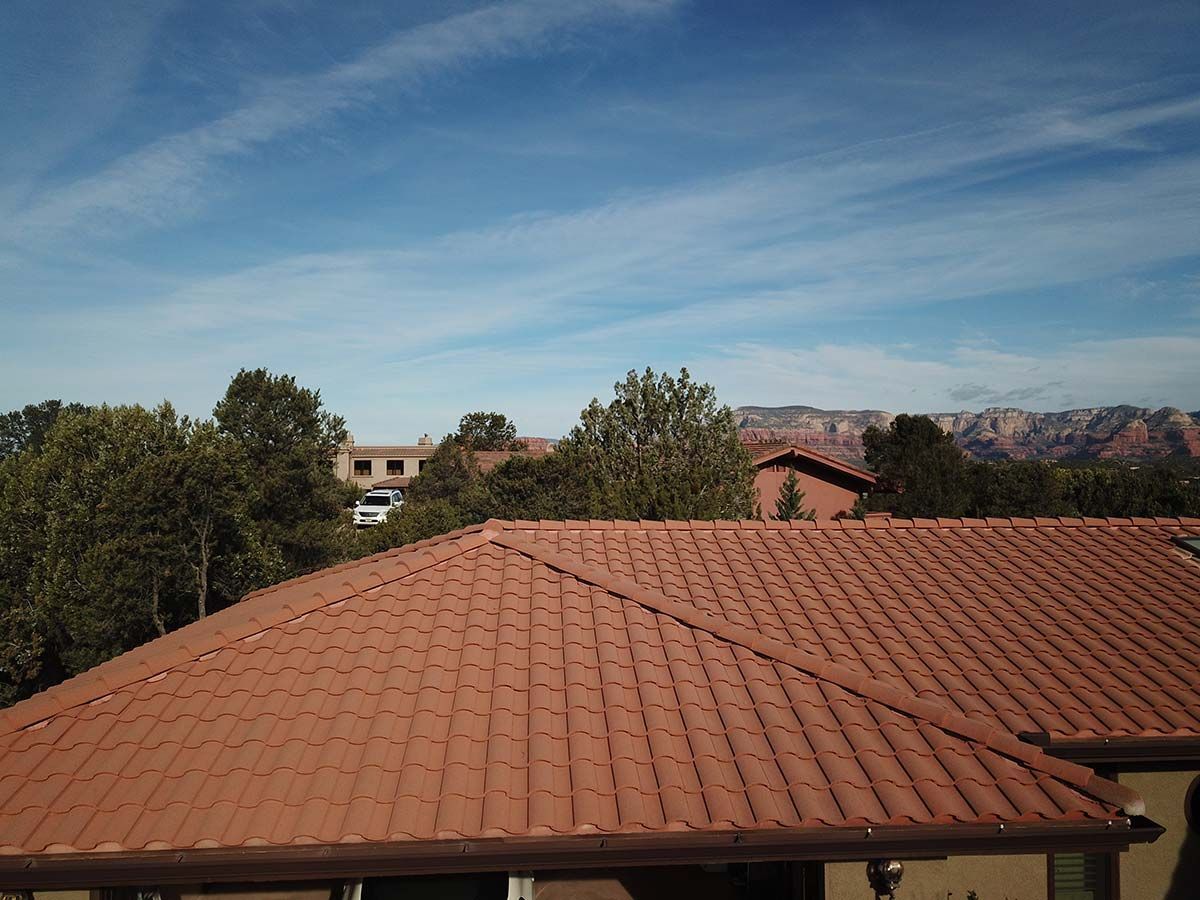 Brown tile roof with trees, buildings, and distant red rock formations under a blue sky.