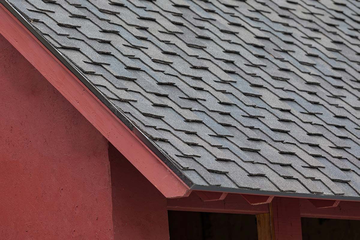 Red building corner with dark gray asphalt shingle roof.