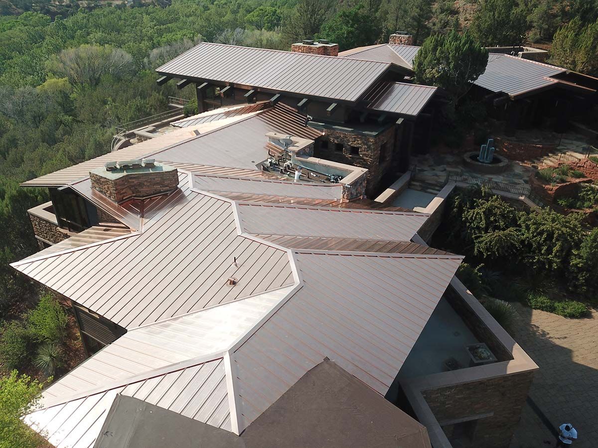 Overhead view of a house with a complex, geometric roof in a wooded area. The roof is copper-colored.