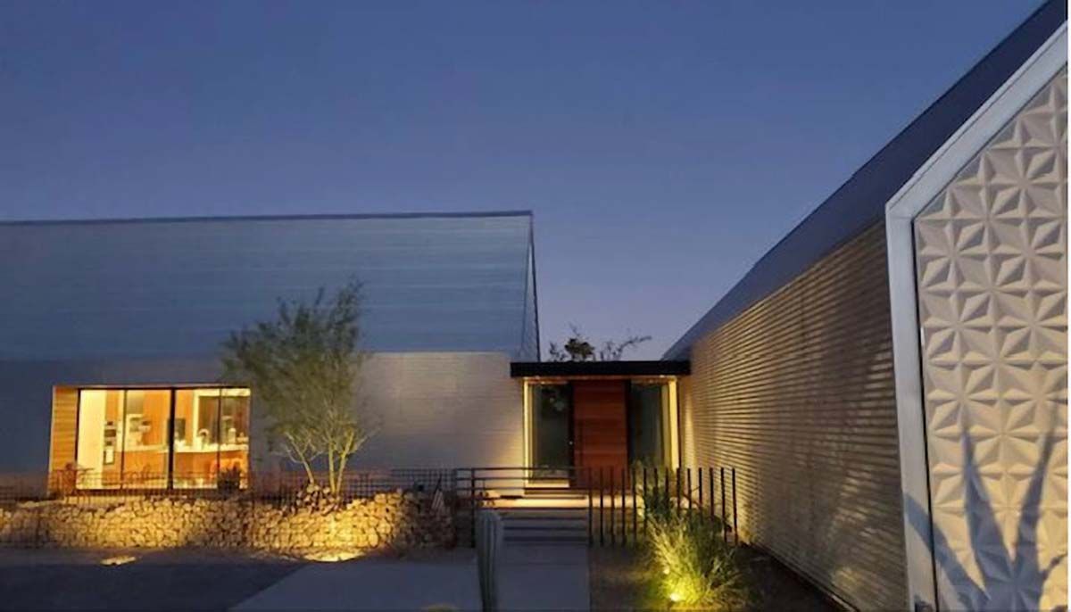 Modern house exterior at dusk, illuminated, with textured wall and entrance path.