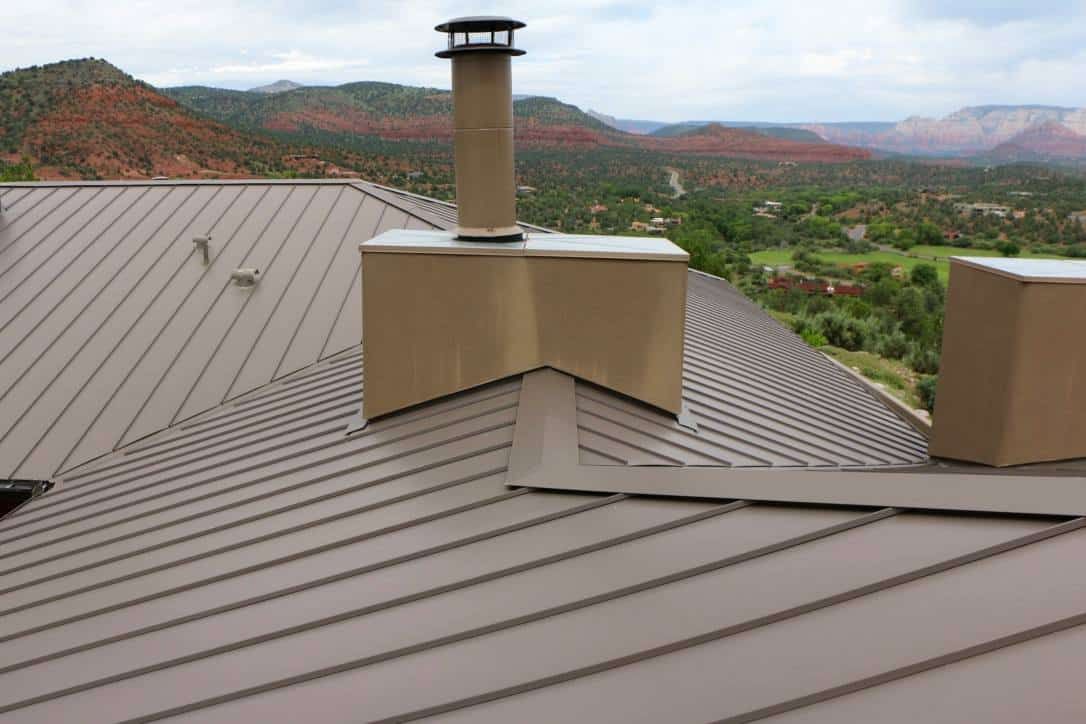 Brown metal roof with a chimney and scenic mountain landscape background.