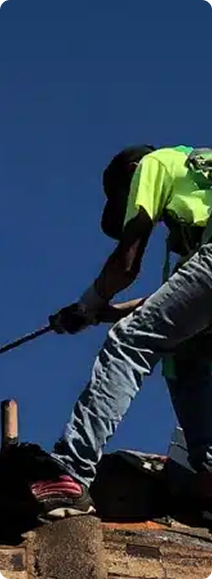 Roofer wearing a safety vest and jeans works on a roof. Clear blue sky.