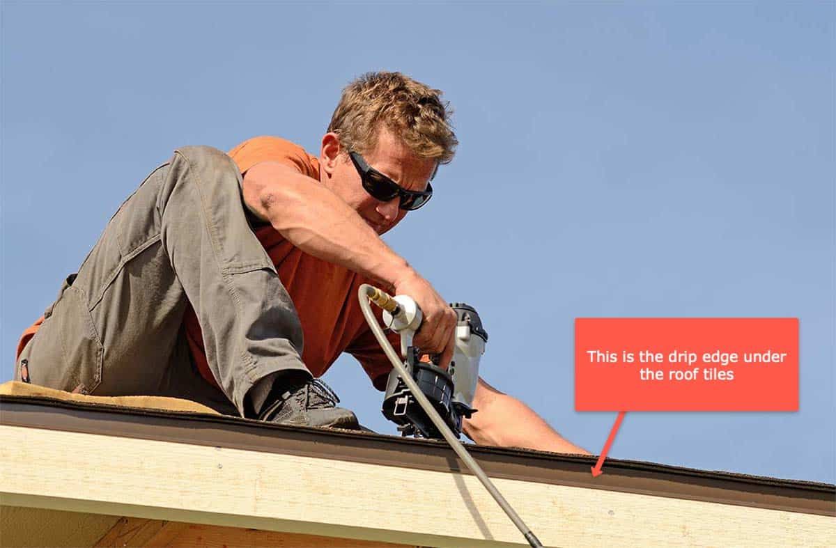 Roofer in white helmet installing flashing around a brick chimney on a tiled roof.