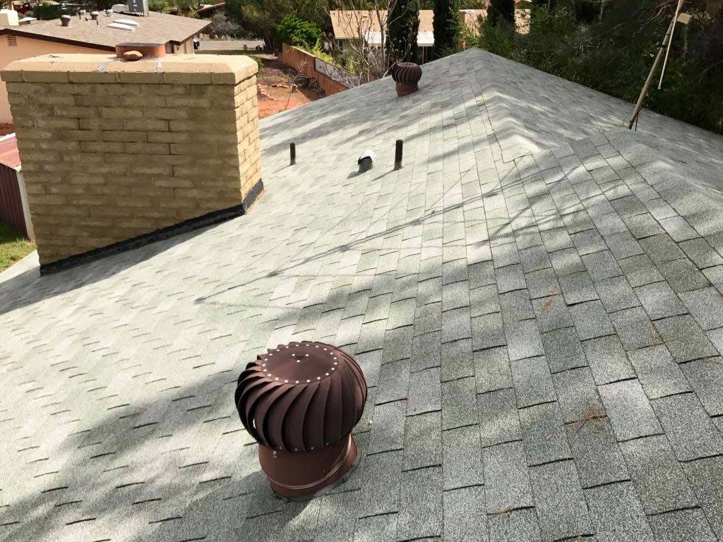 Gray asphalt shingle roof with a brick chimney and a brown turbine vent.