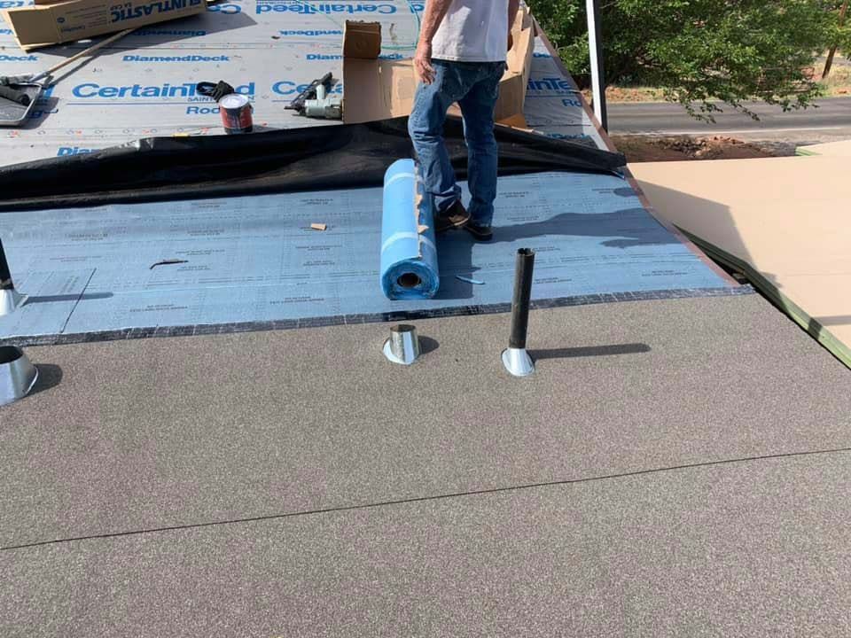 Roofer installing roofing material on a flat roof. Blue roll of material near vent pipes.