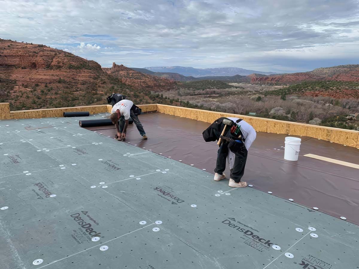 Roofer in white helmet installing flashing around a brick chimney on a tiled roof.