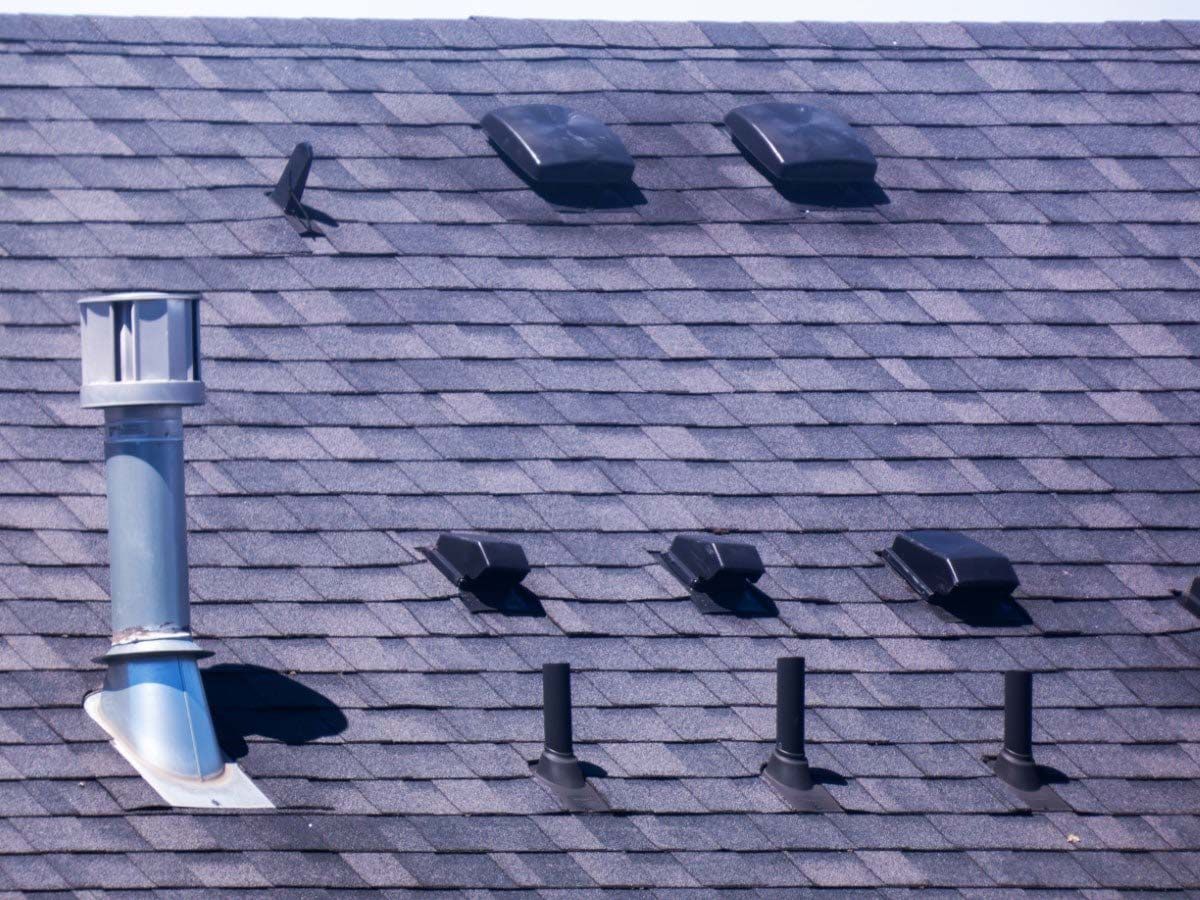 Gray asphalt shingle roof with various vents, including a chimney and several box-shaped vents.