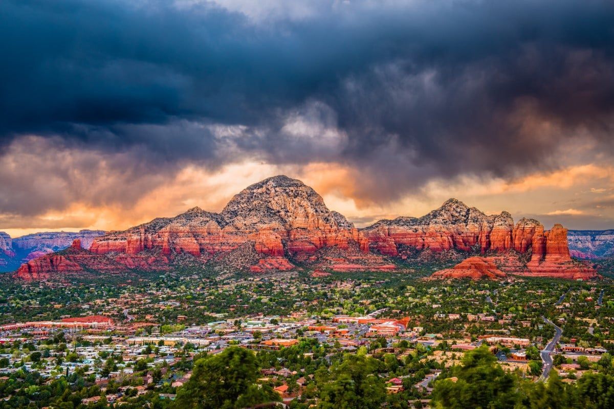 Red rock mountains over a town, under a stormy sky, illuminated by sunset colors.